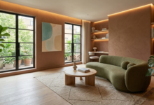 "تصميم غرفة معيشة عصرية تعتمد أحدث صيحات ديكور 2026، تضم أريكة منحنية باللون الأخضر الزيتوني، جدران ترابية دافئة، وطاولة خشبية مستديرة مع إضاءة خفيفة ونباتات طبيعية داخلية."