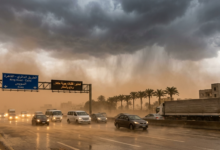 "سيارات تسير على طريق سريع في مصر أثناء عاصفة ترابية (خماسين) مع سحب داكنة وأمطار، وتظهر لوحة إرشادية مكتوب عليها الطريق الدائري - القاهرة السويس."
