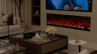 "غرفة معيشة عصرية لعام 2026 بألوان ترابية دافئة، تظهر فيها أحدث ديكورات المنازل العصرية 2026، مع إضاءة مخفية ذكية، قطع أثاث متعددة الوظائف، وجدار نباتي طبيعي يجسد مفهوم الفخامة المستدامة."