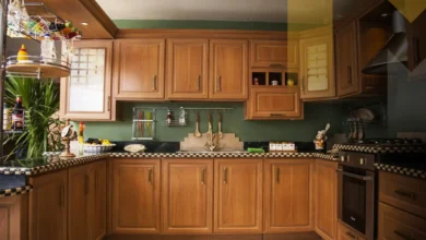 لقطة قريبة تظهر نظام أبواب منزلقة خشبية (Pocket Doors) في منتصف الحركة، تكشف عن مطبخ مخفي مودرن 2026 يتميز بسطح رخامي أبيض فاخر، أجهزة مدمجة بذكاء، وإضاءة LED ناعمة داخل جدار انسيابي.